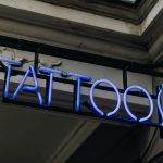 Bright blue neon tattoo sign on a building's exterior wall, ideal for night photography.