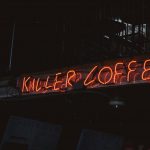 Bright neon sign 'Killer Coffee' in a dimly lit café setting.